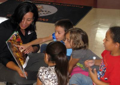 A woman sits on the floor while reading to four children.