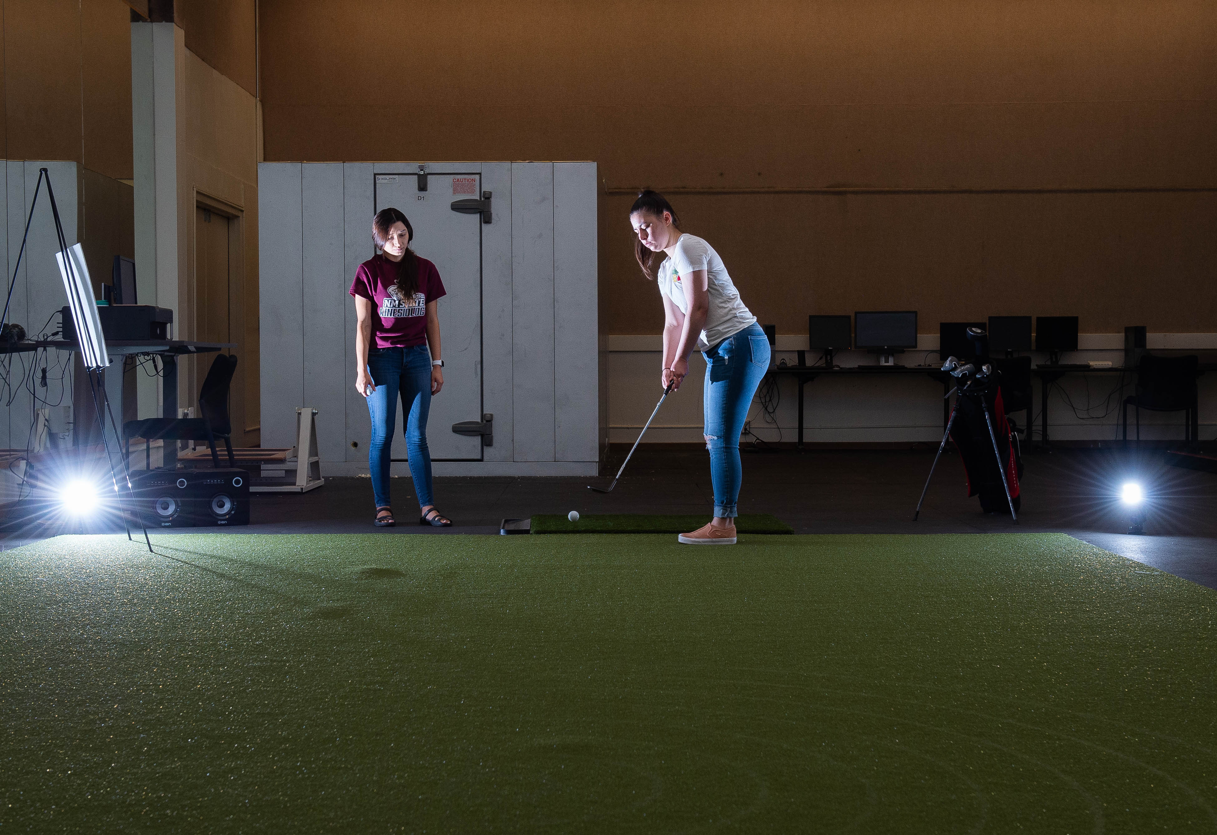 A woman watching another woman hit a ball with a golf club