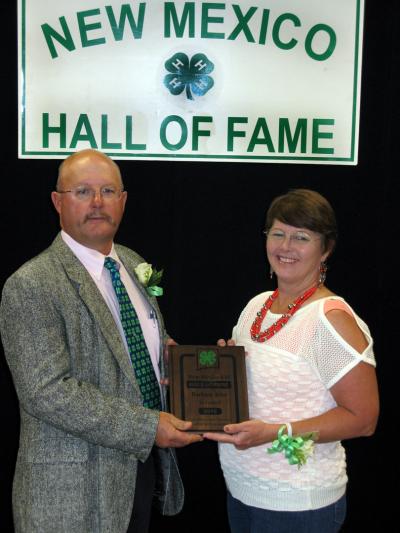 Man and woman, in a white blouse, standing in front of 4-H Hall of Fame sign