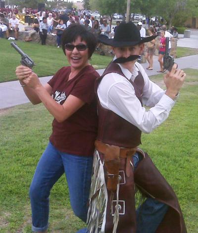 Woman with pistol back-to-back with NMSU cowboy mascot