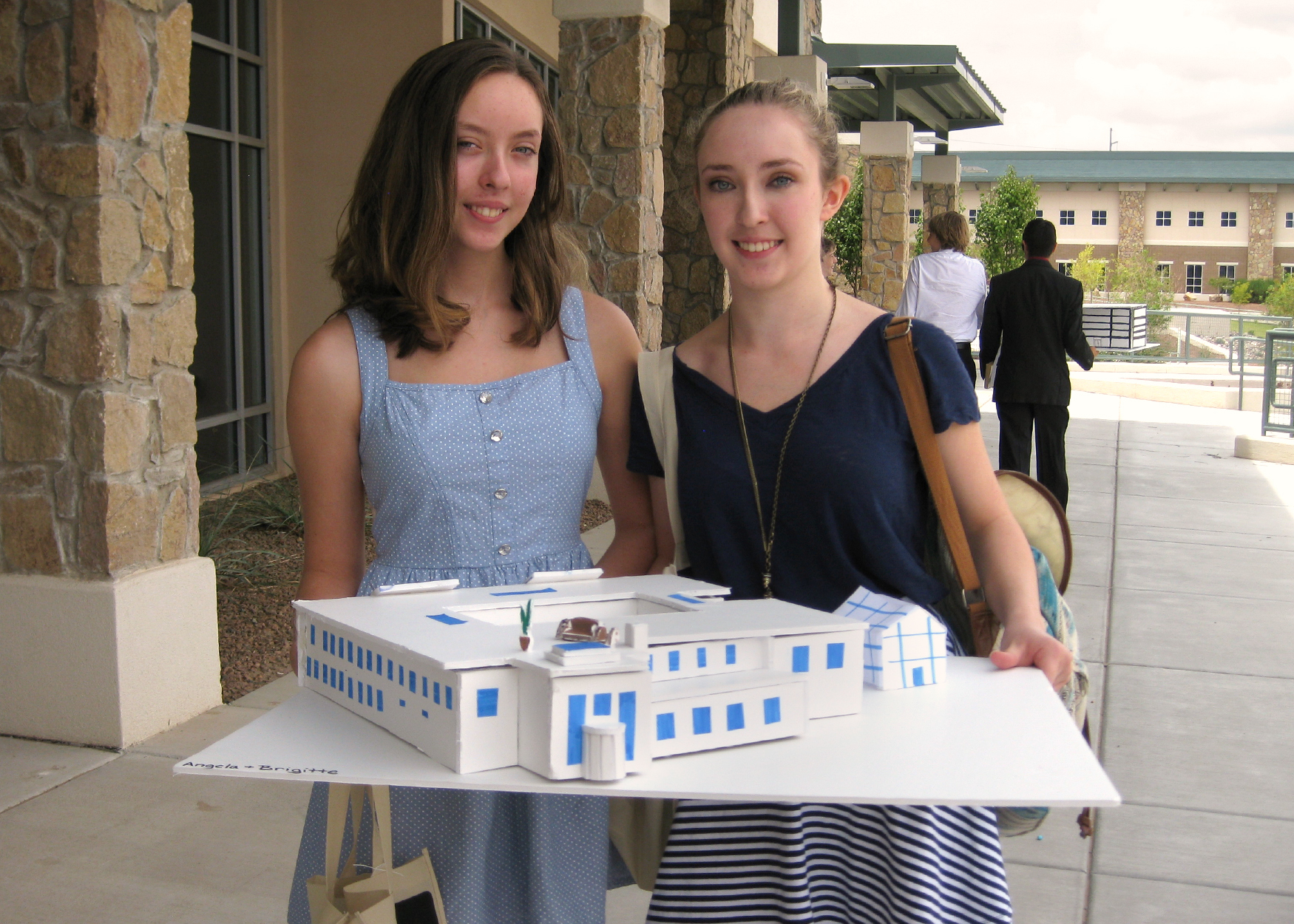 Two young women hold a model of a building concept they designed.