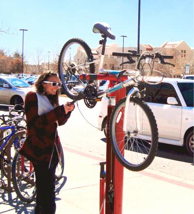 This photo depicts a woman using a red bicycle repair station to complete a repair on her bike. 