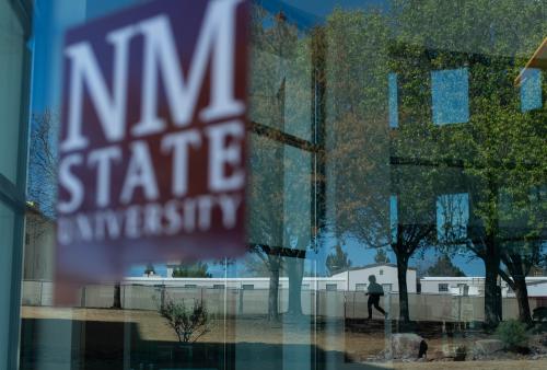 Campus reflection in window with the NMSU logo. 