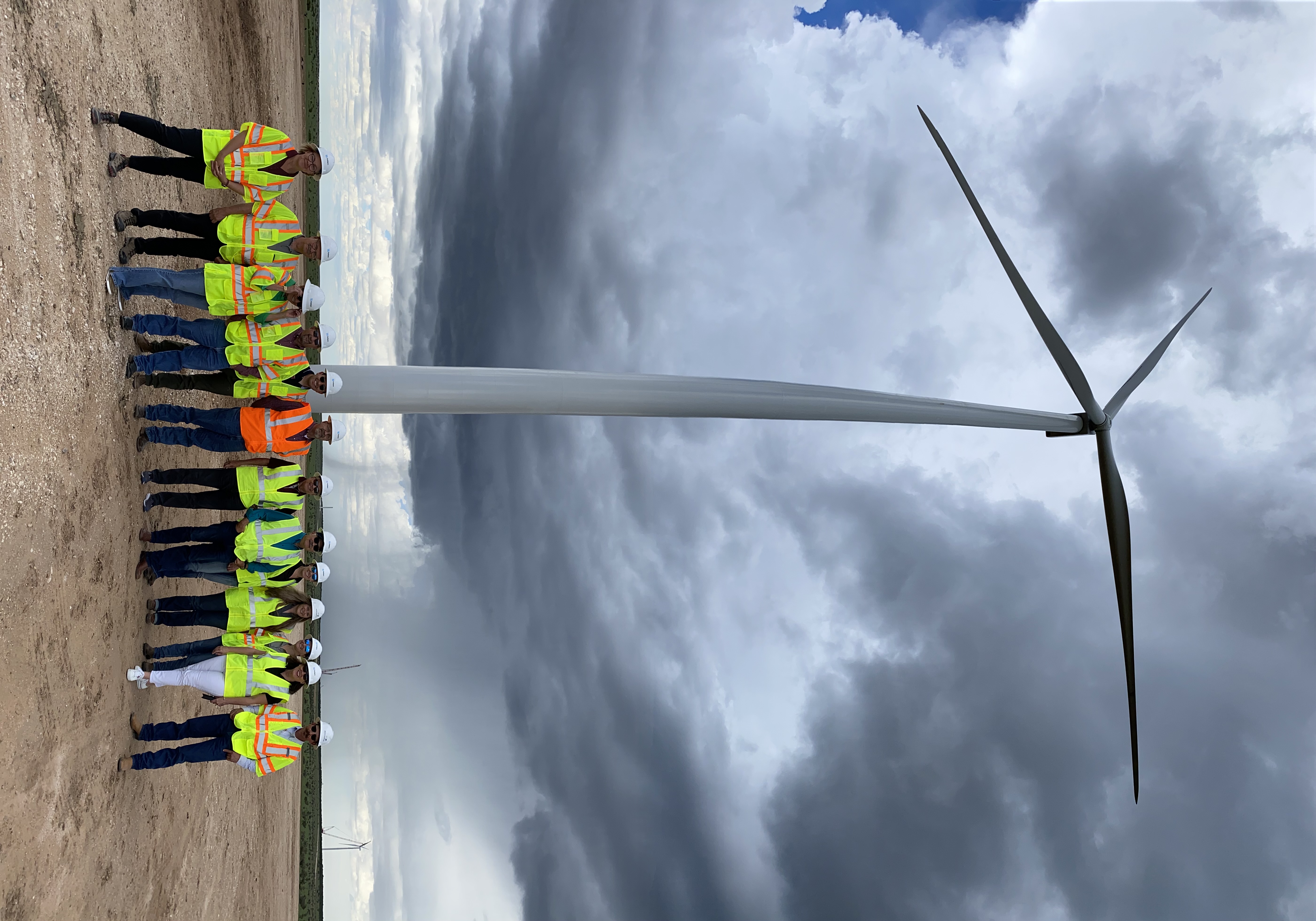 Group of people standing in front of a large wind turbine