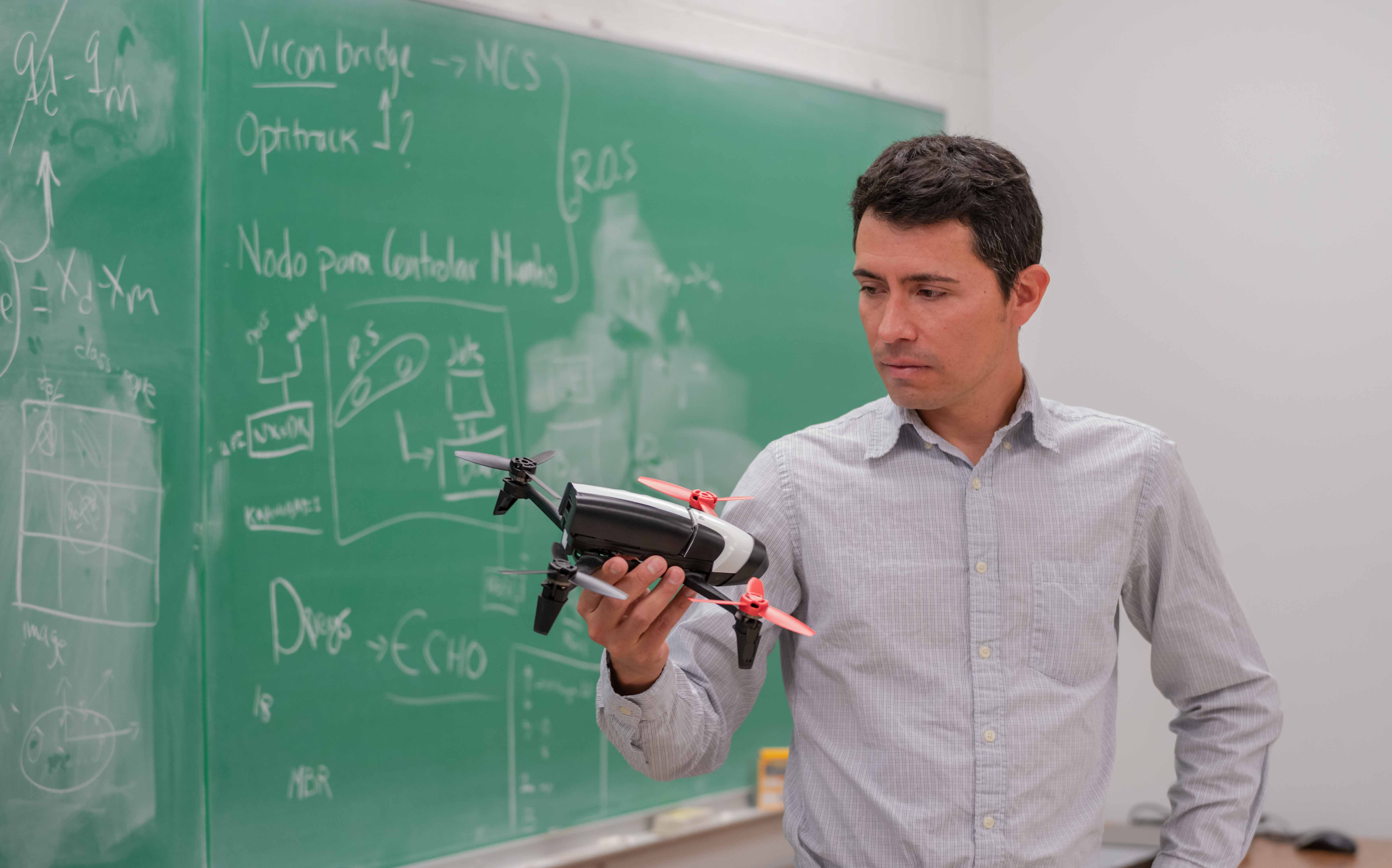 Man standing in front of a chalkboard holding a drone. 