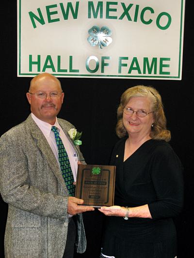 Man and women, in black dress, in front of 4-H hall of fame sign.