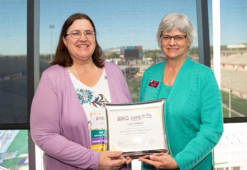 Two women hold an awards plaque. 