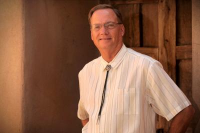 Head and shoulders of man standing against wood and adobe wall background