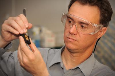  A man in protective glasses examines a tiny device.