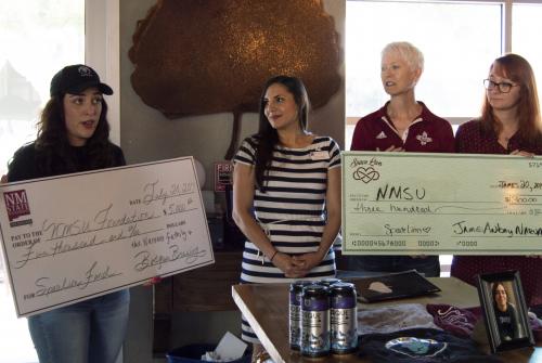 Women stand together with two large checks. 