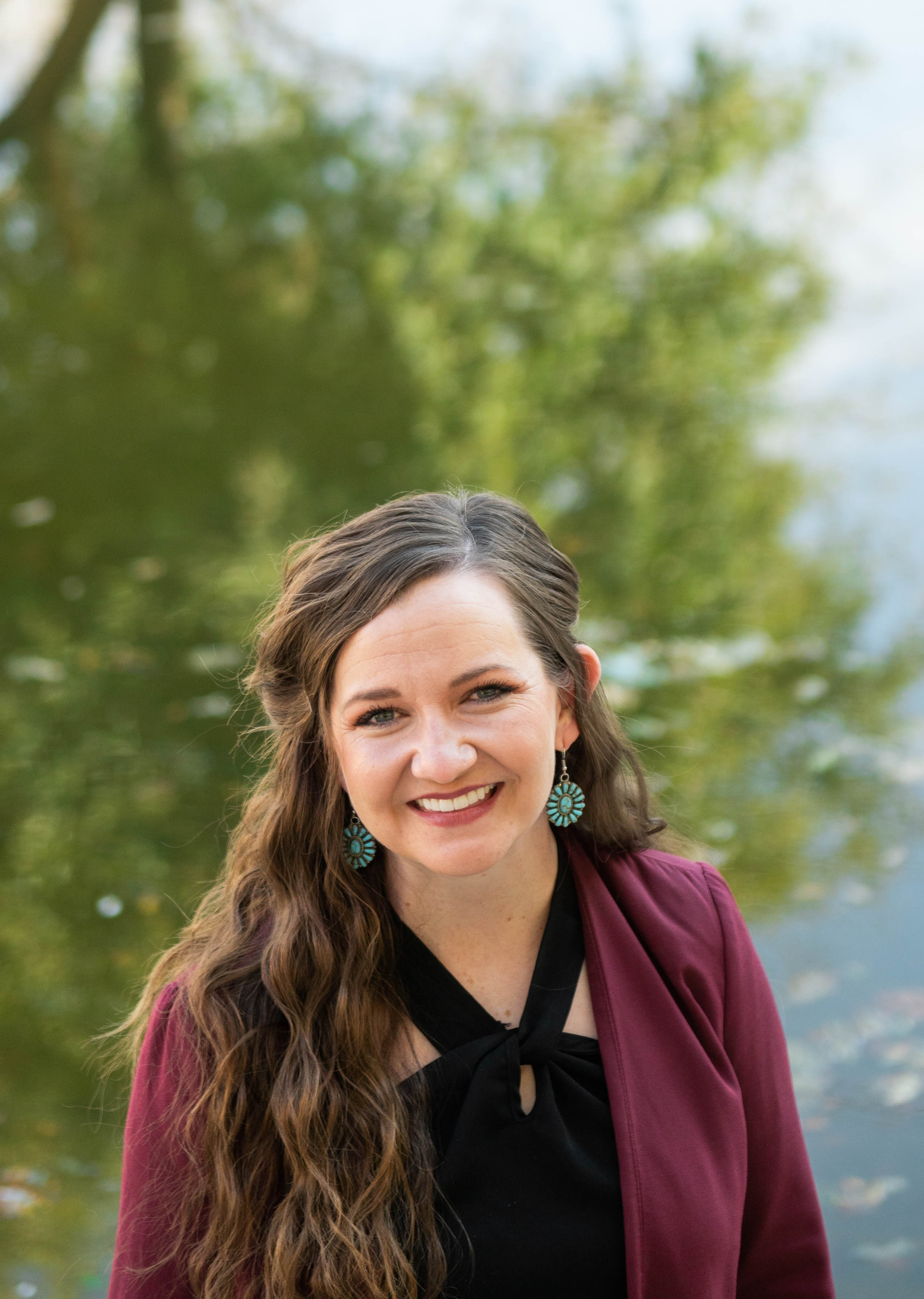 Head and shoulders of a woman outside, in front of a pond.
