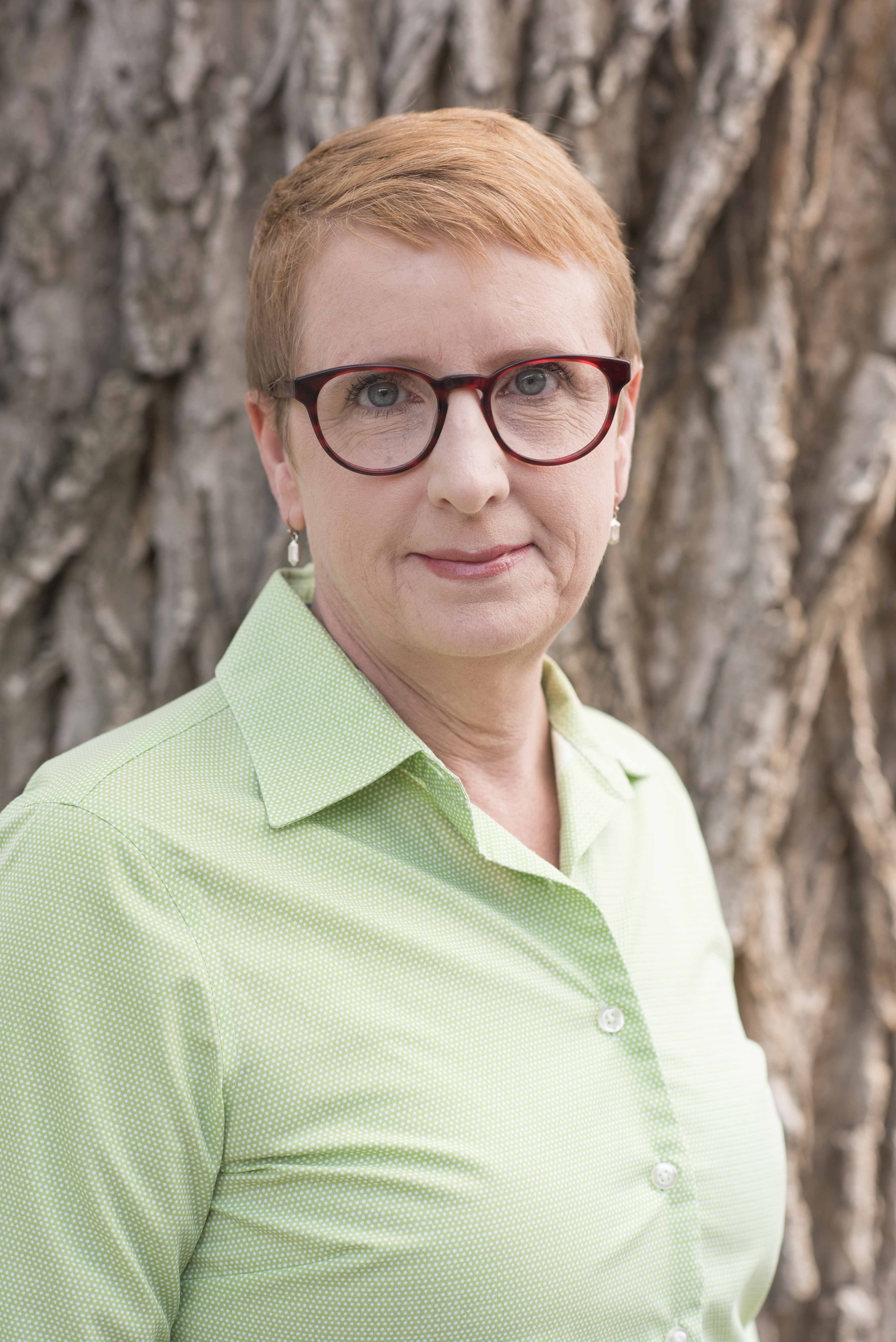 Head and shoulders of a woman standing in front of a tree