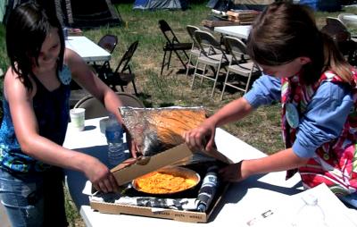 Two girls working on a box that has a yellow dish in middle.