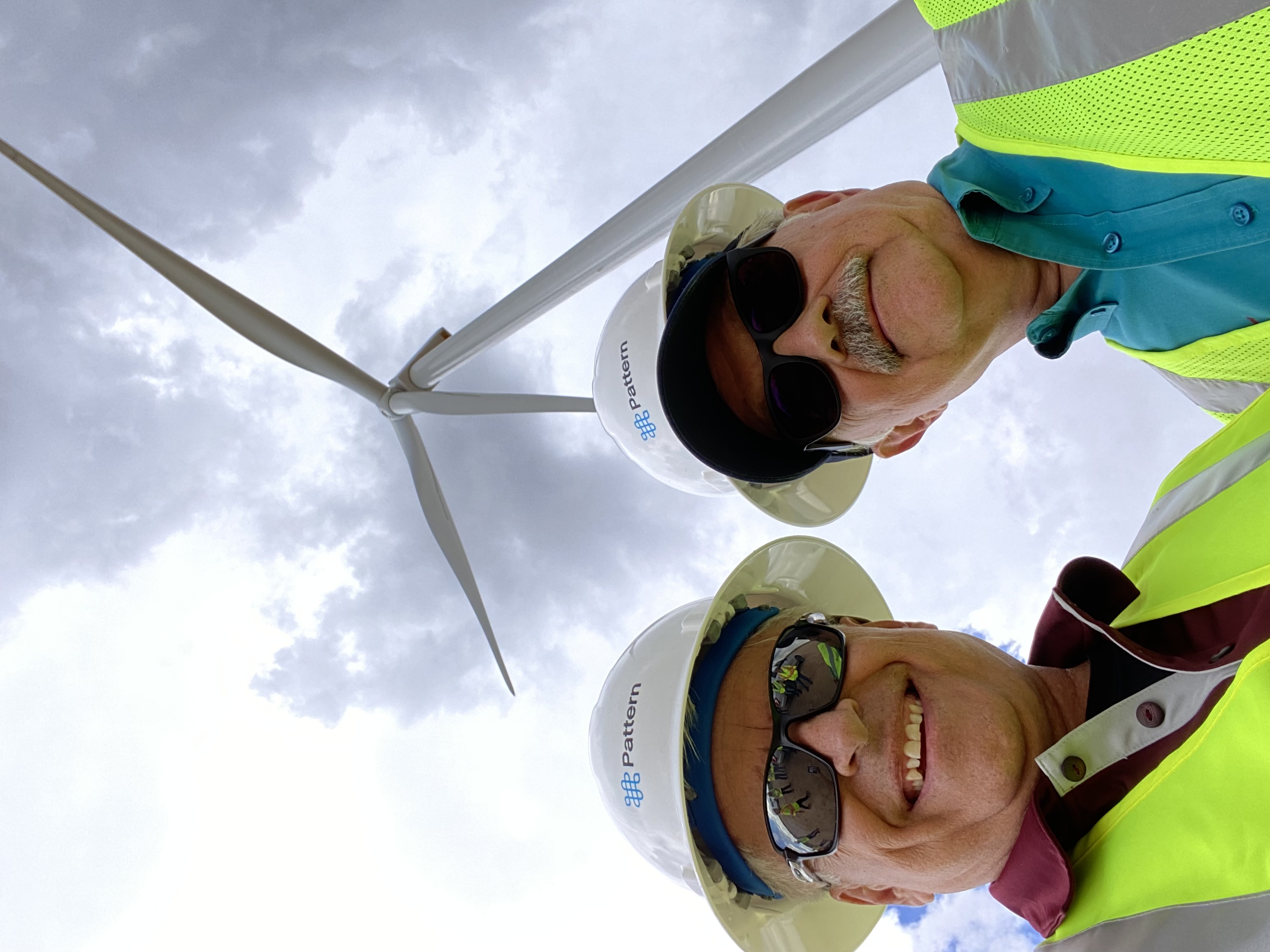 Two men standing in front of a large wind turbine