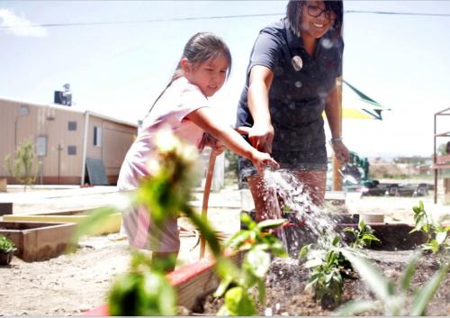 Woman helps a girl water school garden