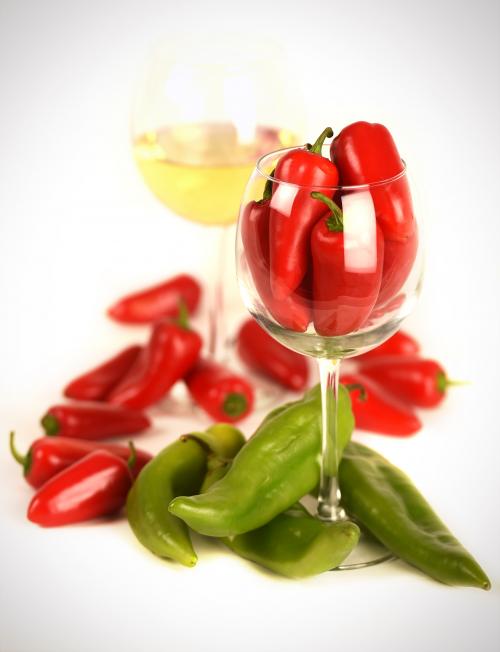 Photo of a wine glass filled with chiles, with chiles scattered around it.