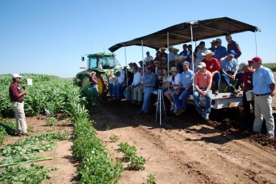 People sitting on hay trailer listening to researcher