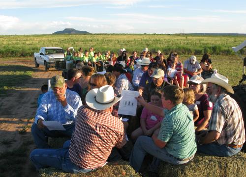 Presenter shares research with group of people sitting on bales of hay